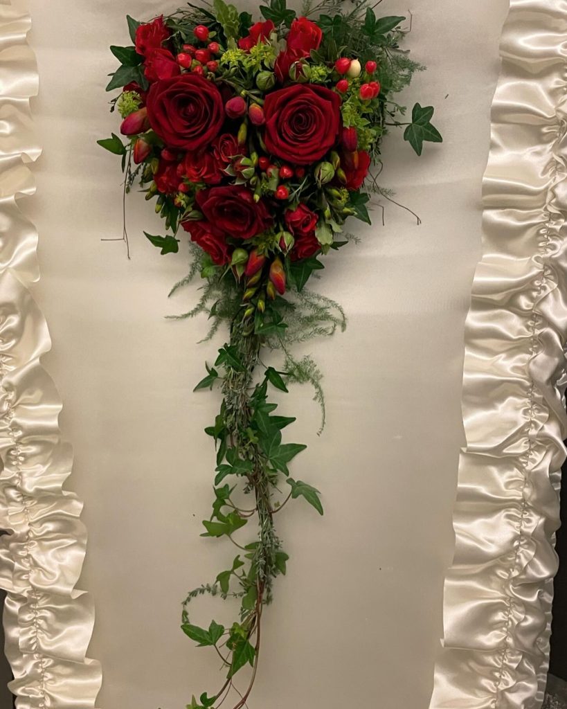 Sargarrangement mit rote Rosen auf einem Sarg.