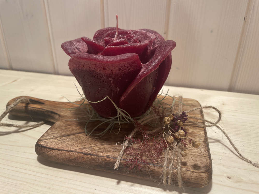 Rote Rosenkerze die ganz wenig ausdekoriert ist auf einem Holzbret.