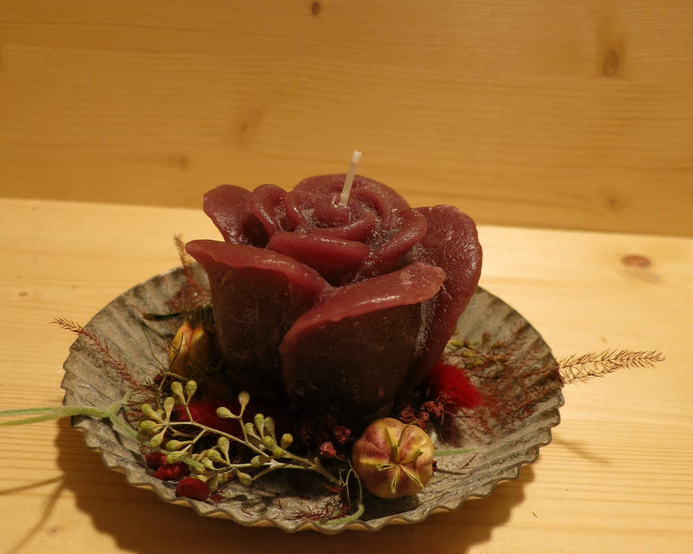 Rosenkerze in Rot auf einem Teller ausgarniert